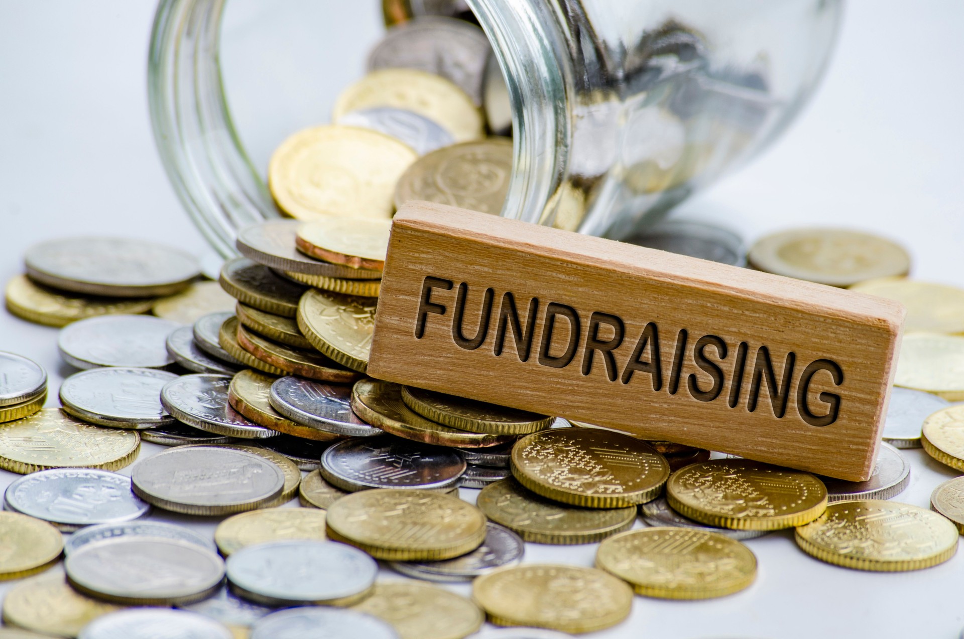 Fundraising text on wooden block with coins and jar background. Charity concept